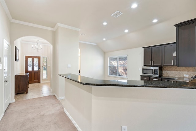 kitchen featuring kitchen peninsula, dark brown cabinetry, light colored carpet, vaulted ceiling, and dark stone countertops