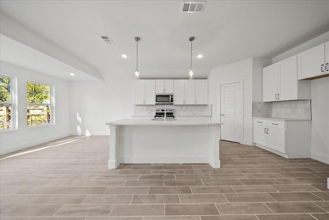 kitchen featuring white cabinetry, appliances with stainless steel finishes, hanging light fixtures, and backsplash