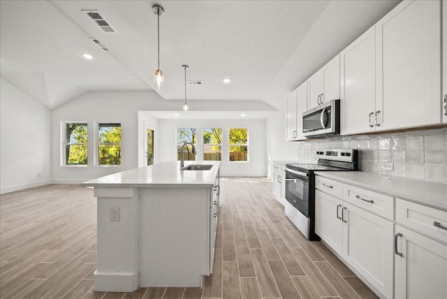 kitchen with appliances with stainless steel finishes, tasteful backsplash, sink, white cabinets, and a center island with sink