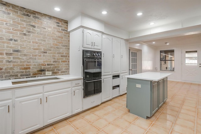 kitchen with a kitchen island, brick wall, black double oven, stovetop, and white cabinets