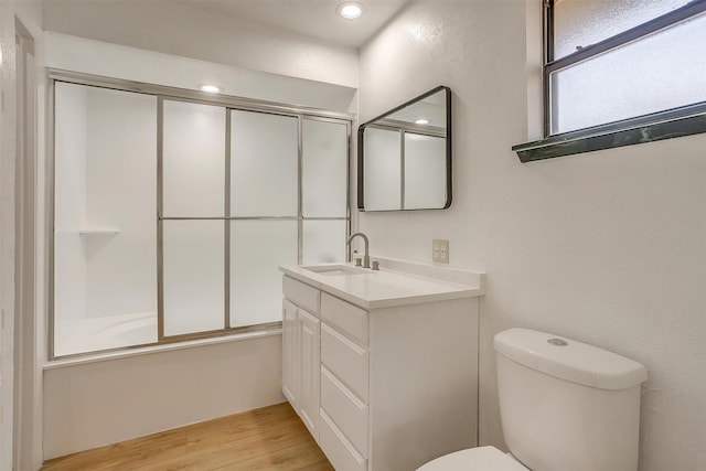 full bathroom with bath / shower combo with glass door, hardwood / wood-style floors, vanity, and toilet