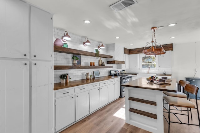 kitchen with white cabinetry, stainless steel stove, pendant lighting, and light wood-type flooring