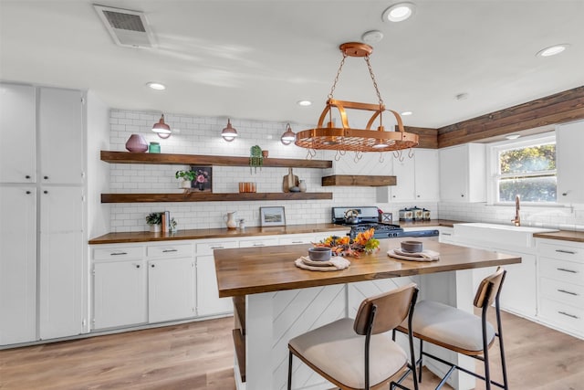 kitchen with wooden counters, decorative backsplash, gas range, white cabinets, and sink