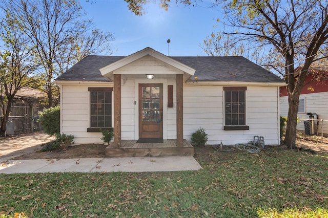 bungalow with a shingled roof, fence, and a front yard