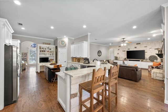 interior space featuring hardwood / wood-style flooring, ornamental molding, a stone fireplace, and ceiling fan with notable chandelier