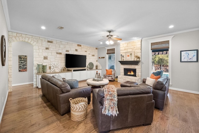 living room featuring crown molding, a stone fireplace, ceiling fan, and light hardwood / wood-style floors