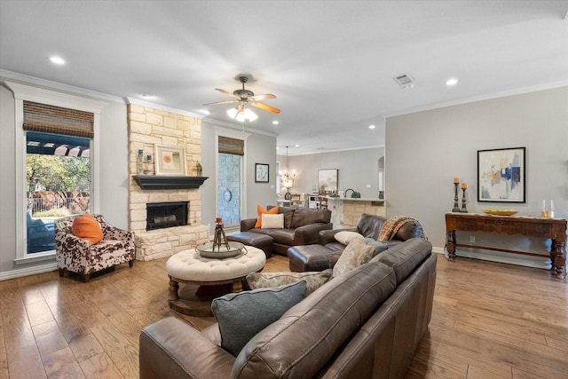 living room featuring ceiling fan, ornamental molding, a stone fireplace, and light hardwood / wood-style flooring