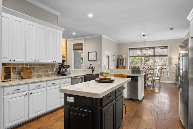 kitchen with appliances with stainless steel finishes, ornamental molding, white cabinets, a kitchen island, and kitchen peninsula