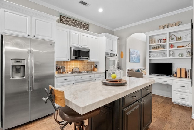 kitchen with light wood-type flooring, ornamental molding, appliances with stainless steel finishes, a kitchen breakfast bar, and white cabinets