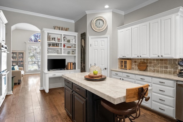 kitchen featuring dark wood-type flooring, a breakfast bar, white cabinetry, a center island, and decorative backsplash