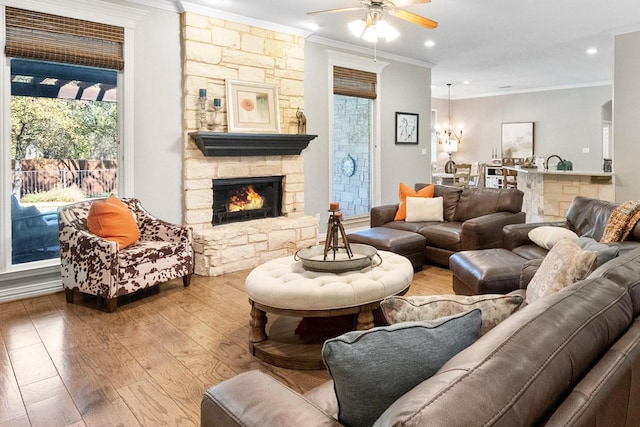 living room with ceiling fan, ornamental molding, a stone fireplace, and light hardwood / wood-style floors