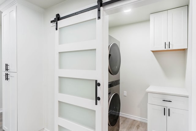 laundry area with cabinets, stacked washer / dryer, a barn door, and light wood-type flooring