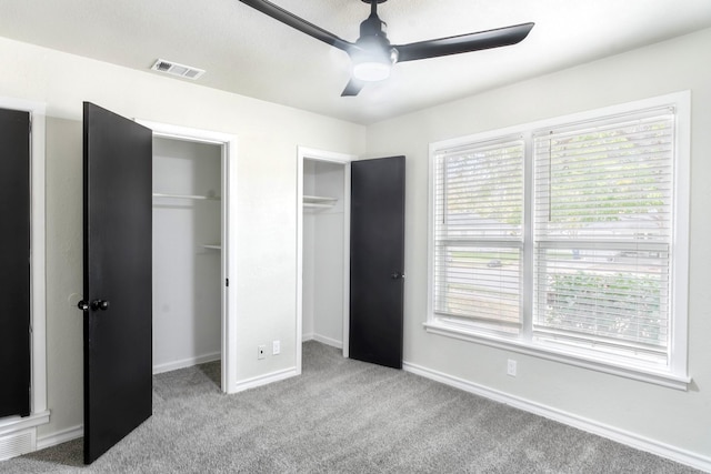 unfurnished bedroom with two closets, light colored carpet, and ceiling fan