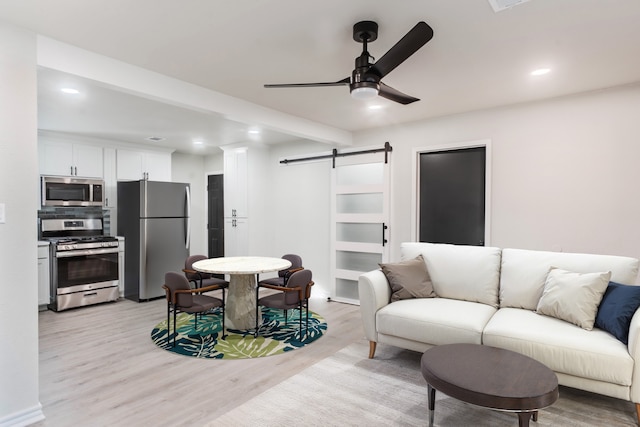 living room with ceiling fan, a barn door, and light hardwood / wood-style floors