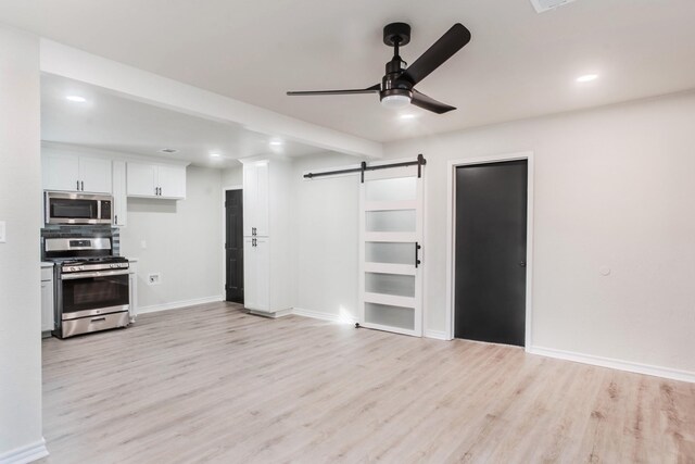 unfurnished living room with ceiling fan, a barn door, and light wood-type flooring