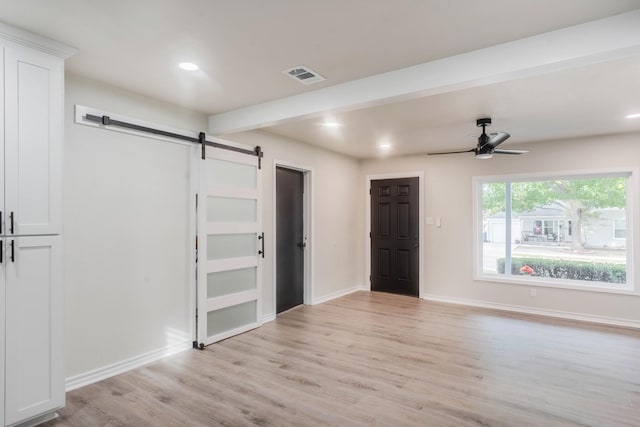 empty room with ceiling fan, a barn door, beam ceiling, and light wood-type flooring