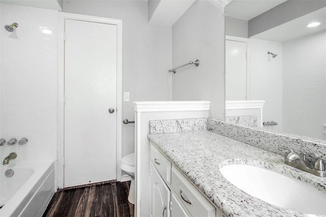 full bathroom featuring wood-type flooring, toilet, tiled shower / bath combo, and vanity