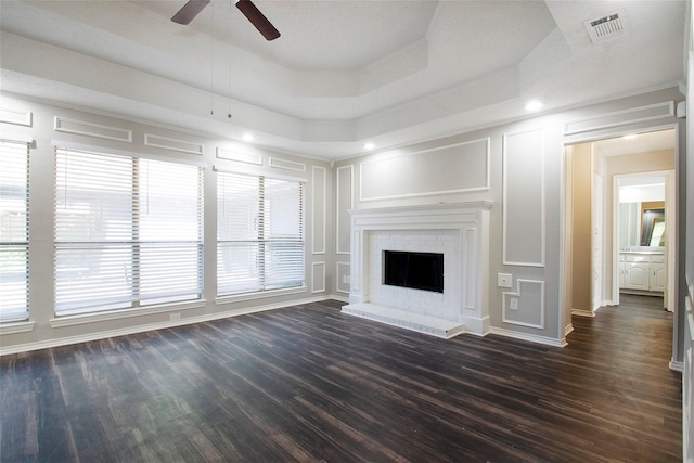 unfurnished living room featuring ceiling fan, a fireplace, dark hardwood / wood-style flooring, and a raised ceiling