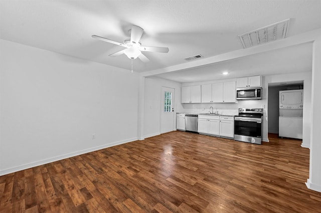 kitchen featuring stacked washer / drying machine, appliances with stainless steel finishes, dark hardwood / wood-style floors, ceiling fan, and white cabinets