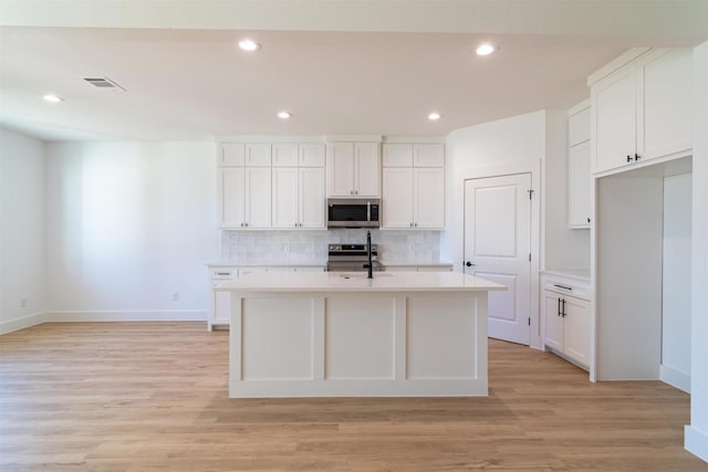 kitchen featuring white cabinets, stainless steel appliances, a center island with sink, and light hardwood / wood-style floors