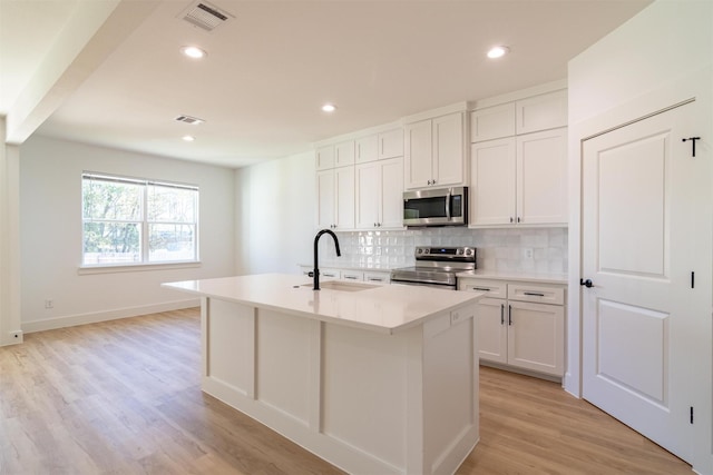 kitchen with white cabinets, an island with sink, stainless steel appliances, and light wood-type flooring