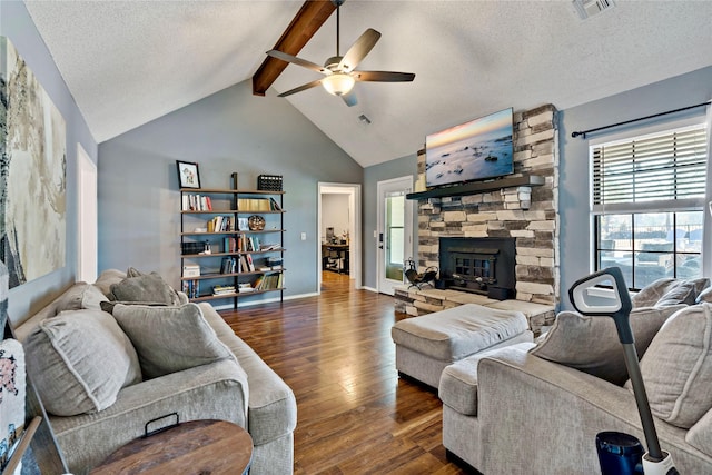 living room featuring dark wood-type flooring, lofted ceiling with beams, a stone fireplace, ceiling fan, and a textured ceiling