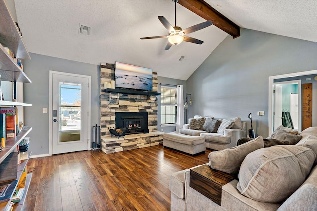 living room with a stone fireplace, hardwood / wood-style flooring, vaulted ceiling with beams, ceiling fan, and a textured ceiling