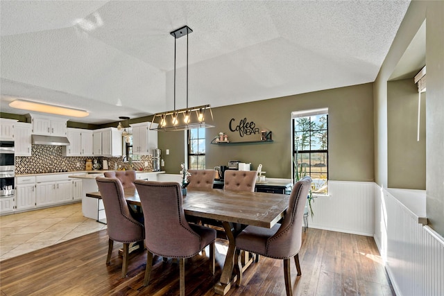 dining area featuring a textured ceiling, light hardwood / wood-style flooring, and lofted ceiling