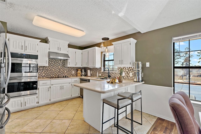 kitchen featuring a kitchen bar, sink, hanging light fixtures, kitchen peninsula, and white cabinets