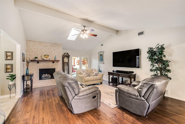 living room featuring a stone fireplace, ceiling fan, dark wood-type flooring, and vaulted ceiling with skylight