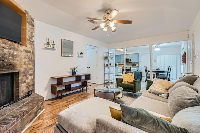 living room with ceiling fan, light wood-type flooring, and a brick fireplace