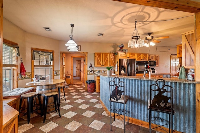 kitchen featuring ceiling fan, hanging light fixtures, stainless steel refrigerator with ice dispenser, a kitchen bar, and kitchen peninsula