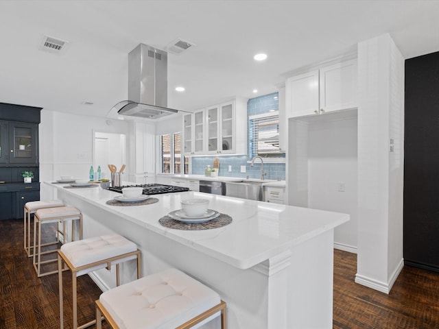 kitchen featuring a center island, white cabinets, appliances with stainless steel finishes, island range hood, and a kitchen bar