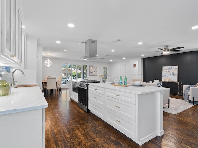 kitchen with dark wood-type flooring, white cabinets, ventilation hood, stainless steel gas stove, and a kitchen island