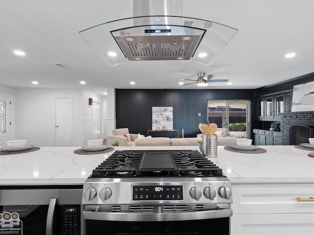 kitchen featuring light stone countertops, a fireplace, stainless steel range, white cabinetry, and island exhaust hood