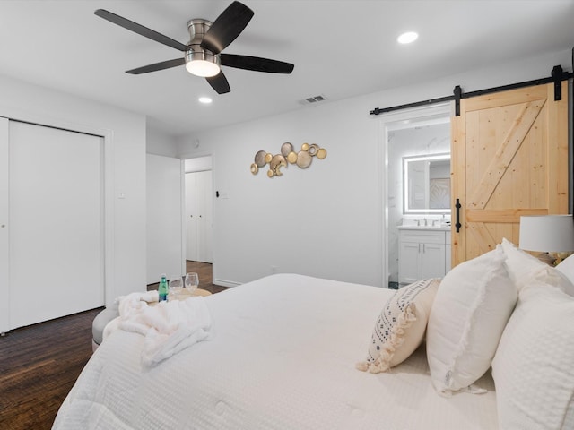 bedroom with ensuite bath, ceiling fan, dark wood-type flooring, sink, and a barn door