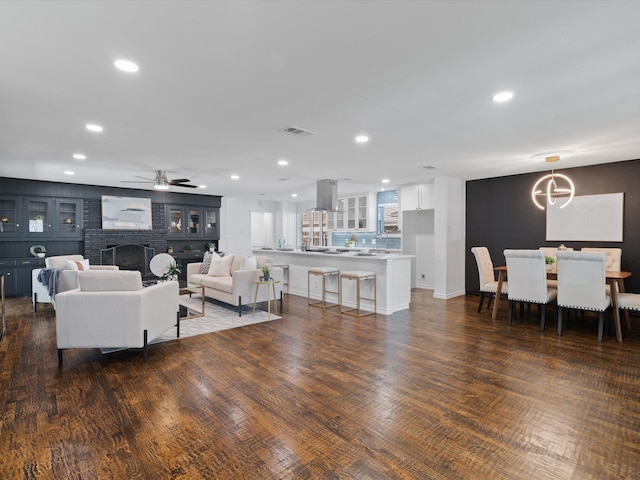 living room with a fireplace, dark wood-type flooring, and ceiling fan with notable chandelier