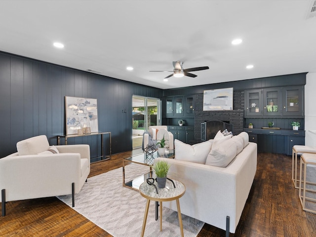 living room featuring dark hardwood / wood-style flooring, a brick fireplace, ceiling fan, and wood walls