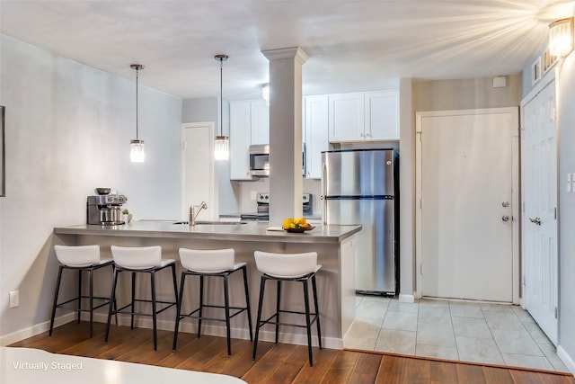 kitchen featuring kitchen peninsula, light wood-type flooring, stainless steel appliances, pendant lighting, and white cabinets