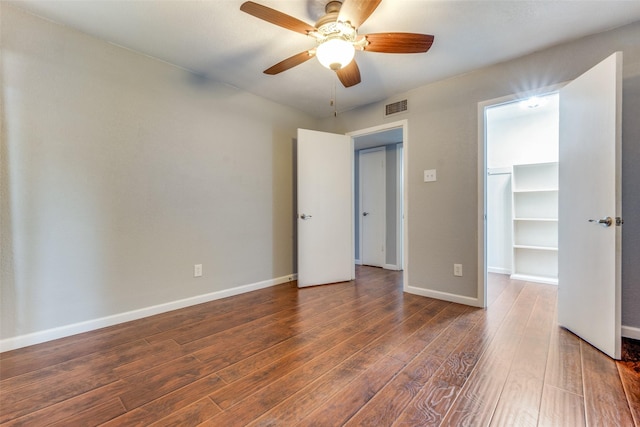 unfurnished bedroom with a walk in closet, dark hardwood / wood-style floors, ceiling fan, and a closet