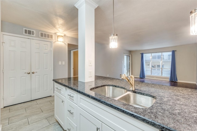 kitchen with pendant lighting, decorative columns, white cabinetry, sink, and dark stone counters