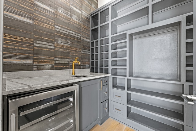 kitchen featuring light stone countertops, light wood-type flooring, gray cabinetry, sink, and wine cooler