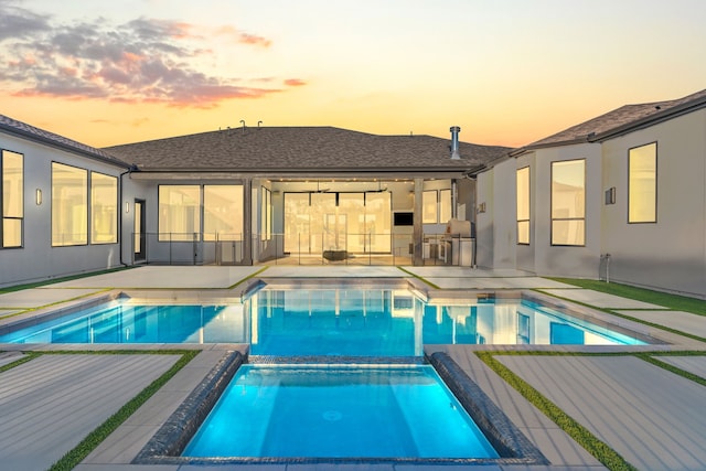 pool at dusk with an in ground hot tub and a patio