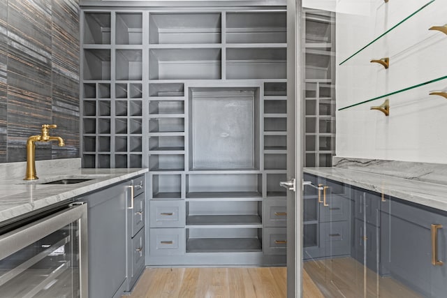 kitchen featuring light stone countertops, sink, beverage cooler, light hardwood / wood-style floors, and gray cabinets