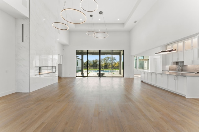 unfurnished living room with a multi sided fireplace, a towering ceiling, light hardwood / wood-style flooring, and sink