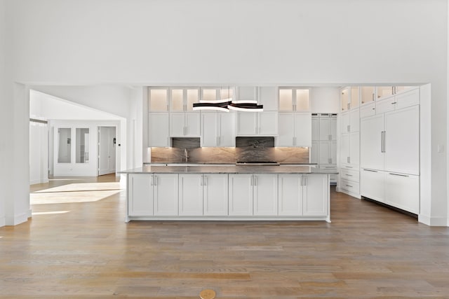 kitchen with a kitchen island with sink, a high ceiling, white cabinets, sink, and light hardwood / wood-style flooring