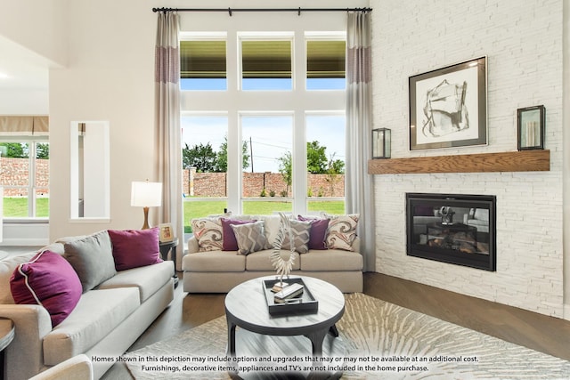 living room with a high ceiling, wood-type flooring, a stone fireplace, and a healthy amount of sunlight