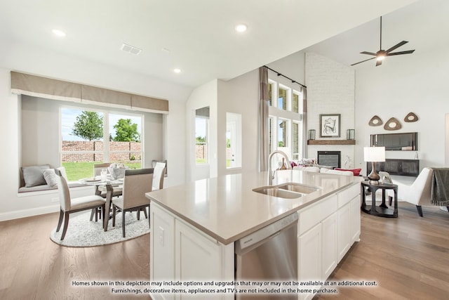 kitchen with sink, a large fireplace, dishwasher, an island with sink, and white cabinets