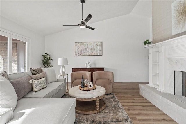 living room with a fireplace, light hardwood / wood-style floors, vaulted ceiling, and ceiling fan