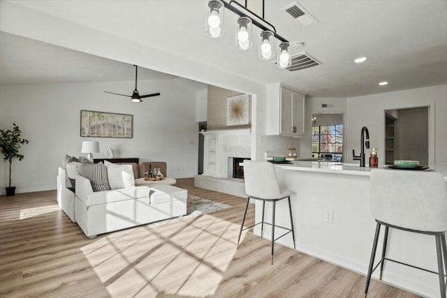 kitchen featuring hanging light fixtures, ceiling fan, a premium fireplace, white cabinetry, and a breakfast bar area